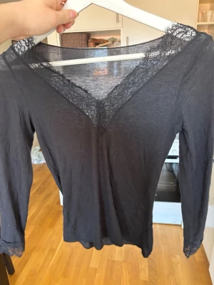 Svart långärmad intimissimi tröja - Svart långärmad topp med v-ringning och fina spetsdetaljer vid halsringning och ärmslut. Tunn och mjuk, perfekt för lager på lager eller som den är. Enkel men elegant design som passar till mycket. Märke intimissimi, storlek M använd ca 2-3 gånger 
