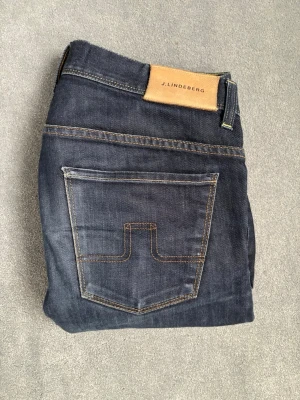 Mörkblå jeans J.Lindeberg - Stilrena mörkblå denim jeans från J.lindeberg. Jeansen är i mycket bra skick och har börjat få riktigt snygga fades. Inga håll eller några andra slitningar på dem. Perfekt nu till våren och på sommar kvällar. Storlek M, måtten: W34 L34. Hör av dig vid minsta fundering!😊