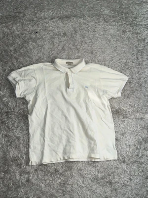 Vit kortärmad pikétröja från burberry - Klassisk vit pikétröja från Gant med korta ärmar och krage. Tröjan har knappar vid halsen och en liten broderad logga på bröstet. Perfekt till en avslappnad men ändå stilren look. För fler frågor/bilder skriv privat. Storlek: M/L