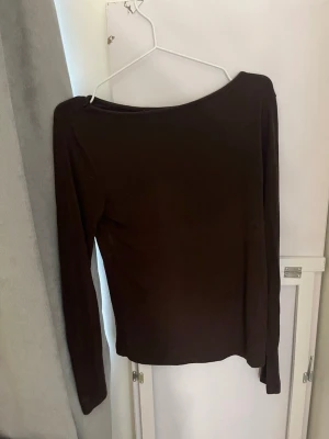Mörkbrun långärmad topp - En enkel och stilren mörkbrun långärmad topp med rund halsringning. Toppen har en smal passform och är tillverkad i ett mjukt material som känns skönt mot huden. Perfekt att matcha med jeans eller kjol för en clean look.