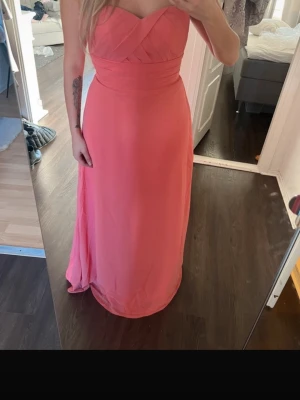 Axelbandslös långklänning i rosa - Säljer en elegant axelbandslös långklänning i en fin rosa nyans. Klänningen har omlott över bysten och markerad midja för en smickrande siluett. Perfekt för bal eller festliga tillfällen.