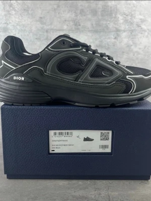 Svarta Dior B30 sneakers - Säljer ett par svarta Dior B30 sneakers med coola reflekterande detaljer och tydlig CD-logga på hälen. Skorna har meshpaneler för extra andningsförmåga och robust sula med Dior-märkning undertill. Snygg design som sticker ut och passar till streetwear.kommer ochså med kvitto 