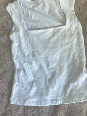 Vit ärmlös linnetopp Gina Tricot - Säljer en enkel och fräsch vit linnetopp från Gina Tricot. Toppen är ärmlös med rundad halsringning och tillverkad i mjuk bomull, perfekt för varma dagar eller som layering-piece.