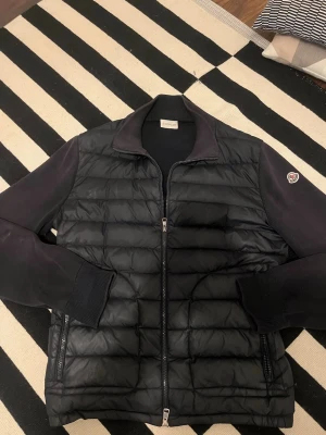 Moncler Cardigan - Säljer nu min finfina cardigan från Moncler. Den är i använt skick, skulle säga 6 eller 7/10. Riktigt bekväm att ha på sig. NFC skann på armen funkar men är inte helt säker på om den är äkta eller inte, därav priset. Dragkedjan på en av fickorna har tyvärr gått sönder men det är inget som inte går att fixa. Har också sytt igen ett hål i samma ficka, syns ej känns ej. Det står XL i jackan men sitter snarare som en M-L. Den är lite solblekt här och där, för lite tydligare bilder skriv gärna i DM! 