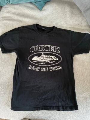 Svart Corteiz t-shirt med tryck - Säljer en svart t-shirt från Corteiz med stort vitt tryck på bröstet där det står 'Corteiz Rules The World' och en grafisk illustration. Klassisk passform och rund hals. Perfekt för dig som gillar streetwear och vill sticka ut. Är använd men i gott skick utan defekter. Pris kan diskuteras.