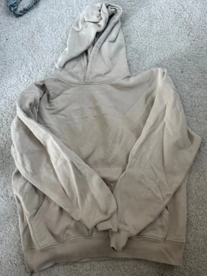 Beige hoodie från Aim'n med huva - Säljer en beige hoodie från Aim'n i storlek XS. Hoodien har broderad Aim'n-logga på bröstet, stor huva och känguruficka framtill. Tillverkad i mjuk bomulls- och polyesterblandning (85% bomull, 15% polyester). Perfekt för en chill och avslappnad stil.