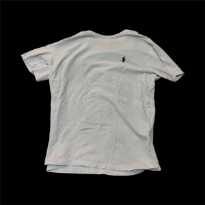 Vit t-shirt från polo Ralph Lauren - Vit t-shirt från Ralph Lauren med klassisk passform och korta ärmar. T-shirten har en broderad marinblå Polo-logga på bröstet och är tillverkad i mjuk bomull. Perfekt basic-plagg med rund halsringning.med ett hål i mitten