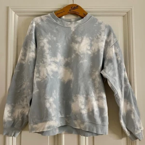 Blå tie-dye hoodie från Monki - Säljer en ljusblå och vit tie-dye hoodie från Monki. Tröjan har en avslappnad passform, rund halsringning och ribbade muddar vid ärmslut och nederkant. Tillverkad i mjukt bomullsmaterial som är skönt mot huden. Perfekt för en chill och trendig look.