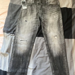 Jack & Jones grå jeans Tapered Mike - Säljer ett par grå jeans från Jack & Jones, modell Mike Tapered. Jeansen har slitna detaljer och en tvättad look med dragkedja i gylfen. Passformen är regular rise och tapered leg. Perfekta för en avslappnad stil. Storlek W-33/L-32. Helt nya och och oanvända köpt för 600kr från Zalando 