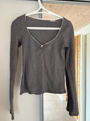 Grå ribbad långärmad topp - Säljer en grå ribbad långärmad topp med v-ringning och spetskant från H&M. Toppen har en söt liten rosett med blomdetalj framtill vid urringningen. 