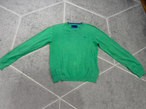 Grön tröja med V-ringning från U.S. Polo Assn. - Snygg grön tröja från U.S. Polo Assn. med V-ringning och diskret logga broderad på bröstet. Tröjan har långa ärmar och ribbade muddar vid ärmslut och nederkant. Perfekt för lager på lager och enkel att matcha med jeans eller chinos.