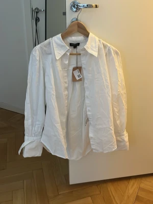 Vit skjorta  - Klassisk vit skjorta från Selected Femme med krage och knappar framtill. Skjortan har lång ärm och är tillverkad i bomull för en skön och luftig känsla. Perfekt att styla till jeans eller kjol för en clean look.