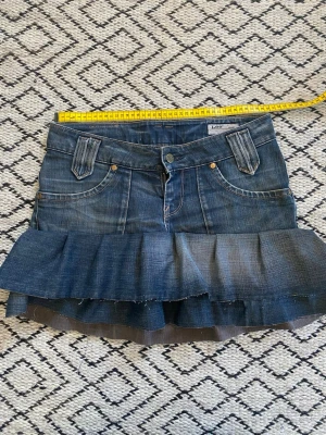 Volangkjol i denim från Lee - Snygg jeanskjol från Lee med volangkant. Cool tvätt på jeanskjolen. Perfekt för en trendig look. Fint omsydda jeans.