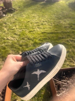 Svarta Axel Arigato sneakers - Svarta sneakers från Axel Arigato i läder med vit sula och broderad fågel på sidan. Jättefint skick. Nypris 2800kr 