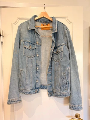 Ljusblå jeansjacka - Säljer en klassisk ljusblå jeansjacka från jack and jones med raka linjer och två bröstfickor med lock och knapp. Jackan har knappstängning framtill och skjortkrage. Perfekt oversized passform :) Säljer den då jag nästan aldrig haft på mig den. 