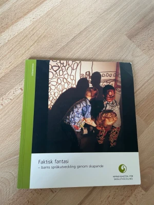 Faktisk fantasi kurslitteratur - Boken 'Faktisk fantasi – barns språkutveckling genom skapande' handlar om barns språkutveckling med fokus på skapande och kreativitet. Omslaget är grönt och vitt med ett foto av barn i aktivitet. Perfekt för dig som pluggar pedagogik eller arbetar med barn.