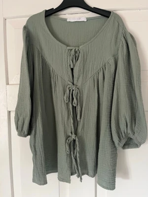 Grön blus med knyt från Sisters Point - Ljusgrön blus från Sisters Point i mjukt, krinklat tyg. Blusen har tre knyt framtill, rund halsringning och trekvartsärmar med resår vid ärmslut. Perfekt för en avslappnad och trendig look.