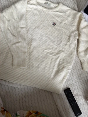 Vit stickad tröja från Moncler - Säljer en stilren vit stickad tröja från Moncler med rund halsringning och Moncler-logga broderad på bröstet. Tröjan har lång ärm och är ribbstickad för en snygg och bekväm passform. Perfekt till säsongens alla outfits. Den har dock tvättats mindre tyvärr. Så passar nog mer en xS-S eller en person som är lite kortare. Eller även barn i storlek 152-170
