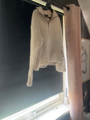 Beige stickad ziptröja från H&M - Mysig beige stickad tröja från lager 157 med dragkedja framtill och hög krage. Tröjan har en avslappnad passform, ribbstickad struktur och långa ärmar. Perfekt för lager på lager och enkel att styla till olika outfits.