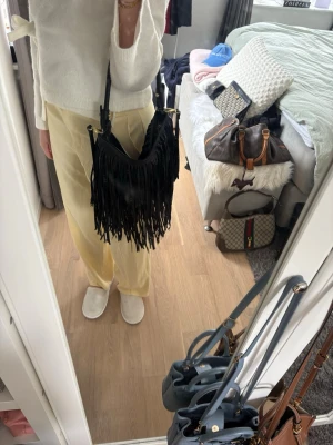 Svart axelväska med fransar - Säljer en svart handväska med långa fransar och axelrem. Väskan har en mjuk, slouchy form och är tillverkad i ett material som liknar skinn. Perfekt för dig som gillar boho-stil och vill ha en unik accessoar till din outfit. Pris går att diskutera vid snabb affär