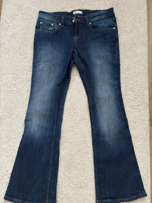 Blå bootcut jeans med slitningar - Säljer ett par blå bootcut jeans med snygga slitningar och kontrastsömmar på bakfickorna. Jeansen har klassisk femficksmodell och är tillverkade i denim. Perfekta för dig som gillar en avslappnad men trendig look.
