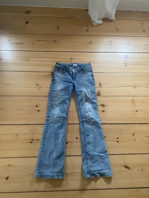 Blå bootcut jeans med detaljer på fickorna - Säljer ett par blåa bootcut jeans med låg/medellåg midja. Väldigt stretchigt material. Fickor med detaljer. Lite slitna/missfärgade nertill