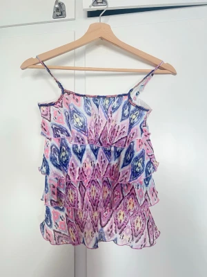 Mönstrad volanglinnetopp med pärlor - Säljer en färgglad linnetopp med tunna axelband och flera volanger. Perfekt inför sommaren💗💗storlek EUR 128, men skulle säga att den passar xs/xxs🥰