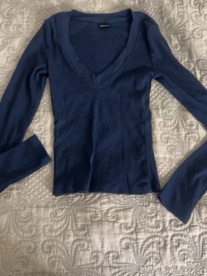 Mörkblå ribbad V-ringad tröja - Slimmad mörkblå tröja med djup V-ringning och långa ärmar. Tröjan är ribbstickad och har en enkel, stilren design som passar perfekt till jeans eller kjol. Materialet känns mjukt och följsamt mot kroppen.