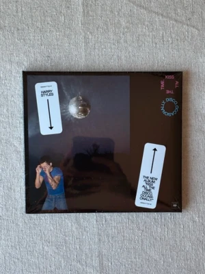 Harry Styles CD-album - Säljer ett CD-album av Harry Styles med svart omslag och spegelboll på framsidan. Omslaget har tryck i vitt och rosa samt en bild på artisten. Perfekt för dig som gillar popmusik och vill ha en fysisk skiva till samlingen. Helt nytt! Inte öppnat