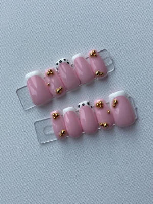 Rosa press-on naglar med pärldetaljer - Snygga press-on naglar i ljusrosa med vit fransk tipp, svarta prickar och små guldfärgade pärlor. Naglarna har en rundad form och trendig design som sticker ut. Perfekt för dig som vill ha en unik och kreativ nagelstil.