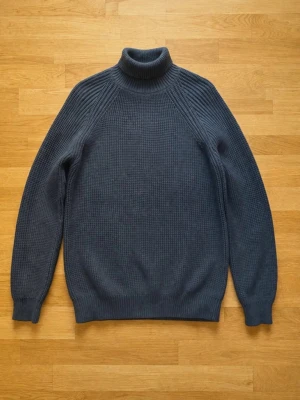 Mörkblå polotröja från Casual Junkies - Mörkblå stickad polotröja från Casual Junkies i storlek S. Tröjan har en hög polokrage, lång ärm och ribbstickade muddar vid ärmslut och nederkant. Perfekt för kalla dagar och enkel att matcha med jeans eller kjol.