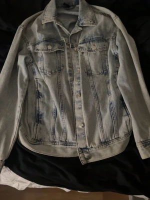 Ljusblå  jeansjacka H&M - Säljer en ljusblå jeansjacka från H&M med tvättad effekt och klassisk krage. Jackan har två bröstfickor med lock och knappar! väl använd men skulle inte säga några tydliga tecken på användning