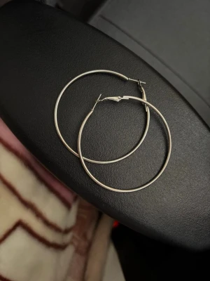 Stora silvriga hoops örhängen - Säljer ett par stora, tunna hoops örhängen i silverfärgad metall. Klassisk rund form som ger en clean girl vibe. Tyvärr vet jag inte vart jag köpt de från då det va ett tag sedan. Anledningen till att jag säljer de är på grund av att jag inte använder mig av silver😞