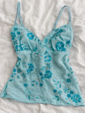 Ljusblå Y2K topp med pärlor & broderi – Ibiza vibe - Superfin ljusblå Y2K-topp med blombroderier och små pärldetaljer. Figurnära modell med tunna band som sitter jättefint på.  Ger riktig Ibiza / beach club / sommar i Europa-känsla 🌊 Perfekt till semester, festival, utekväll eller middagar i solnedgången. Så snygg med vita linnebyxor, lågmidjade jeans eller en flowy kjol.  • Skick: mycket bra • Storlek: XS–S • Färg: ljusblå • Stil: Y2K / Ibiza / coquette  Snabb frakt 💌 