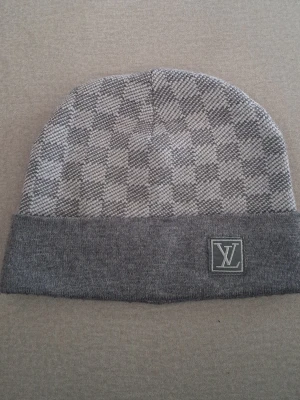 Grå mössa med rutmönster - Snygg grå mössa n med klassiskt rutmönster Tillverkad i mjukt stickat material som känns skönt mot huden. Perfekt accessoar för att lyfta din look.