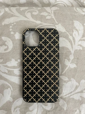 Svart mobilskal By Malene Birger iPhone12 - Snyggt svart mobilskal från By Malene Birger med beige grafiskt mönster. Skalet har en matt finish och är gjort i tålig plast som skyddar mobilen. 