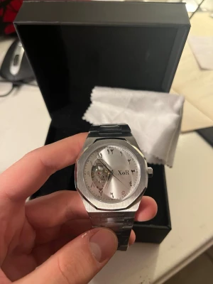 XoR Obsucra 41mm Silver/Grå HELT NY - Stilren klocka från XoR i borstat silverfärgat 316L rostfritt stål med unikt urverk synligt på urtavlan. Klockan har arabiska siffror, rund urtavla och länkarmband i metall. Kommer helt ny med originalbox. Plasten är på eftersom den är sprillans ny.