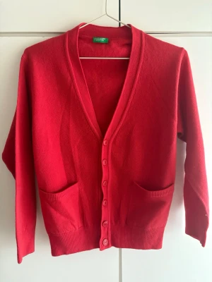 Röd kofta från Benetton - Snygg röd kofta från United Colors of Benetton med v-ringning, knäppning framtill och två fickor. Tillverkad i 100% mjukt cachmire som känns skönt mot huden. Perfekt att slänga över en t-shirt eller topp för en enkel men stilren look. Köptes för några år sedan och jag har aldrig använt den. Tror den kan passa till både tjejer och killar. Pris kan diskuteras 🥰