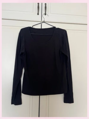 Svart långärmad topp i bomull - En enkel och stilren svart långärmad topp med rund halsringning. Tillverkad i mjuk bomull som känns skön mot huden. Perfekt att matcha med jeans eller kjol för en clean look.
