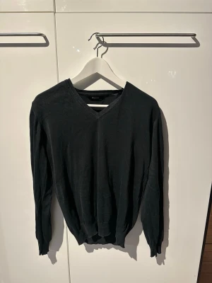 Svart v-ringad stickad tröja  - Svart stickad tröja från Sand med v-ringad hals och långa ärmar. Tröjan har ribbade muddar vid ärmslut och nederkant. Enkel och stilren modell som är lätt att matcha.
