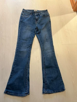 Blå bootcut jeans från Anna Carter - Snygga blå bootcut jeans från Anna Carter med klassisk femficksmodell och dragkedja. Jeansen har en utsvängd passform nedtill och är tillverkade i mjuk denim. Perfekta för dig som gillar retrovibbar och vill ha ett par bekväma jeans med cool siluett.