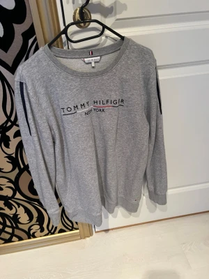 Grått sett Tommy Hilfiger S - Grå sweatshirt och byxor från Tommy Hilfiger med tryckt logga och texten 'New York' på bröstet. Tröjan har rund halsringning och långa ärmar med diskreta mörkblå detaljer på axlarna. Perfekt för en avslappnad och stilren look.