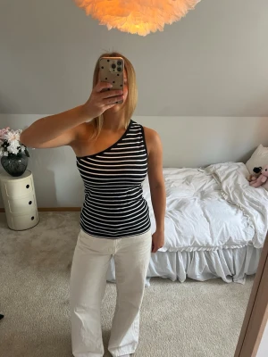Randig oneshoulder topp i svart och vitt - Snygg randig topp med oneshoulder-design i svart och vitt. Tight passform och ärmlös, perfekt för dig som vill sticka ut. Mjuk och stretchig känsla, passar till många olika stilar.