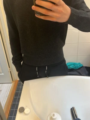 Mörkgrå stickad tröja med rund hals - En stilren mörkgrå stickad tröja med rund hals och långa ärmar. Tröjan har ribbstickade muddar vid ärmslut och nederkant, vilket ger en snygg passform. Perfekt för lager-på-lager och enkel att matcha med olika outfits. Helt oanvänd