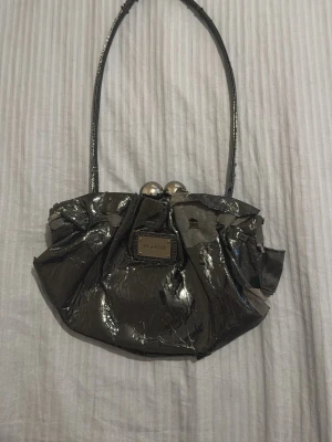 Svart glansig kuvertväska Topshop - Snygg svart kuvertväska från Topshop i glansigt material med metallic finish. Väskan har en unik rynkad design, silverfärgade kulor som lås och ett smalt axelband. Perfekt för att lyfta din outfit med en cool touch.