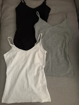 3-pack baslinnen i olika färger - Tre stilrena linnetoppar i svart, grått och vitt med smala axelband och enkel design. Perfekta att matcha till olika outfits och superbekväma tack vare mjukt bomullsmaterial. från lager 157 har använt 1 gång 