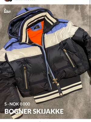 Bogner pufferjacka med huva - Snygg pufferjacka från Bogner i svart, blått och vitt med orange innerfoder. Jackan har huva, dragkedja framtill, två fickor med guldfärgade dragkedjor och ribbade muddar med ränder. Perfekt för kalla vinterdagar och riktigt sportig vibe. Haft den att åka skidor i så inte använt den så mycket💕 får inte användning för den längre så säljer den💕 köpt 2020 på kaisers i Sälen💕 nypris var 17 000kr💕 