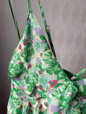 Grön blommig sommarklänning - Säljer en söt kort grön klänning med blommigt mönster i lila och rosa toner. Klänningen har smala axelband och v-ringad halsringning. Materialet känns lätt och luftigt, perfekt för varma dagar. Den är köp på Vinted. Lite sliten men syns inte alls! Korsad i ryggen.