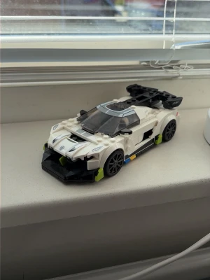 Vit LEGO sportbil med svart vinge - Säljer en cool sportbil byggd av LEGO, främst i vitt med svarta detaljer och en stor bakvinge. Bilen har genomskinligt tak, svarta fälgar och små inslag av limegrönt och blått. Perfekt för dig som gillar bilar och LEGO-byggsatser.