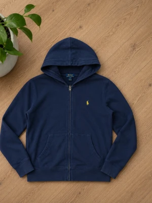 Mörkblå hoodie från Polo Ralph Lauren - Mörkblå hoodie med dragkedja från Ralph Lauren. Klassisk design med huva, känguruficka och gul broderad logga på bröstet. Perfekt för en avslappnad och stilren look. Tillverkad i mjukt bomullsmaterial.